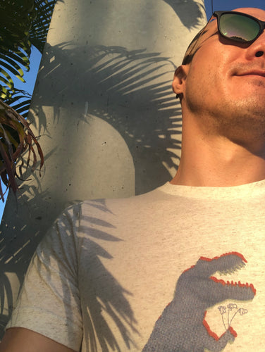 Nate DeWaele, is modeling the t-shirt he designed.  The t-shirt has anaglyph glitch dinosaurs holding flowers. The graphic is in halftone texture for natural blending into the fabric.